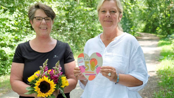 Zwei Frauen halten einen Blumenstrauß und eine Karte in ihren Händen